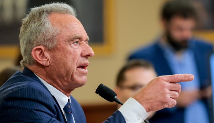 Older man in a blue pinstripe suit testifies, pointing as he speaks into a microphone.