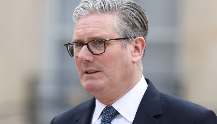 Portrait of a middle-aged man with gray hair and glasses in a dark suit and patterned tie outdoors.